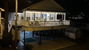 Een huis aan het water met een overdekt terras, buitenmeubels en een garage.
