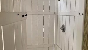 Een wit metalen hekwerk met verticale latten en een deurklink.