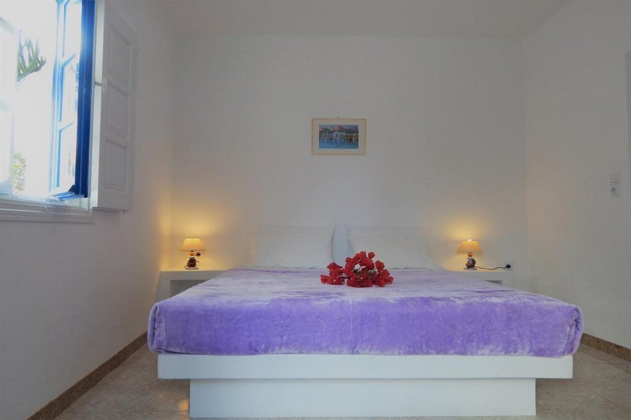 A bedroom with a bed, two bedside lamps, a window with blue curtains, and a small framed picture on the wall.