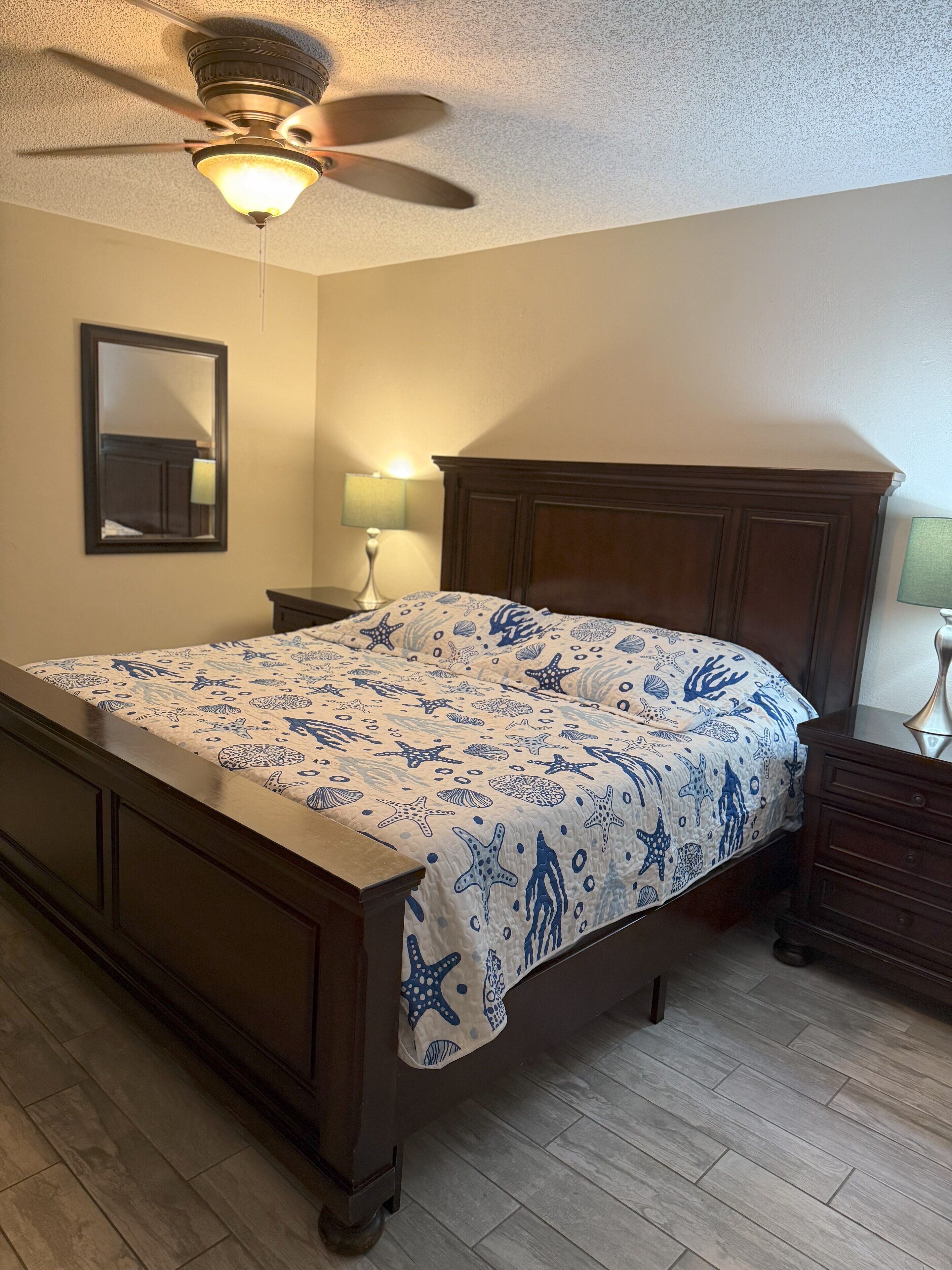 Un dormitorio con cama, ventilador de techo, mesita de noche, lámpara y cómoda.