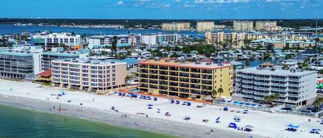 A coastal cityscape with a beachfront hotel featuring multiple floors, a pool area, and a view of the sea.