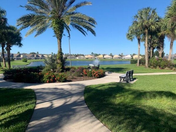 A pathway leading to a bench with a view of a lake and houses in the background.