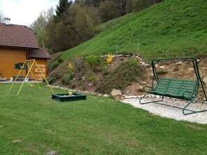 Relax in a serene outdoor setting with a traditional house, green swing set, and sandbox.