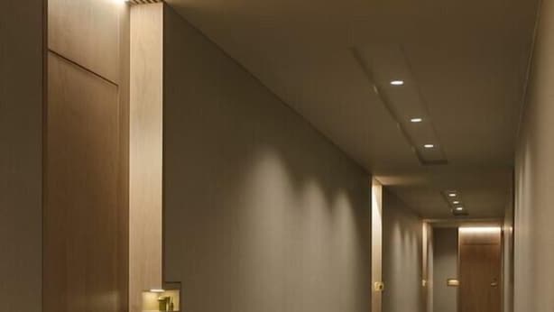 Un long couloir étroit, doté de portes en bois et d’un éclairage encastré.