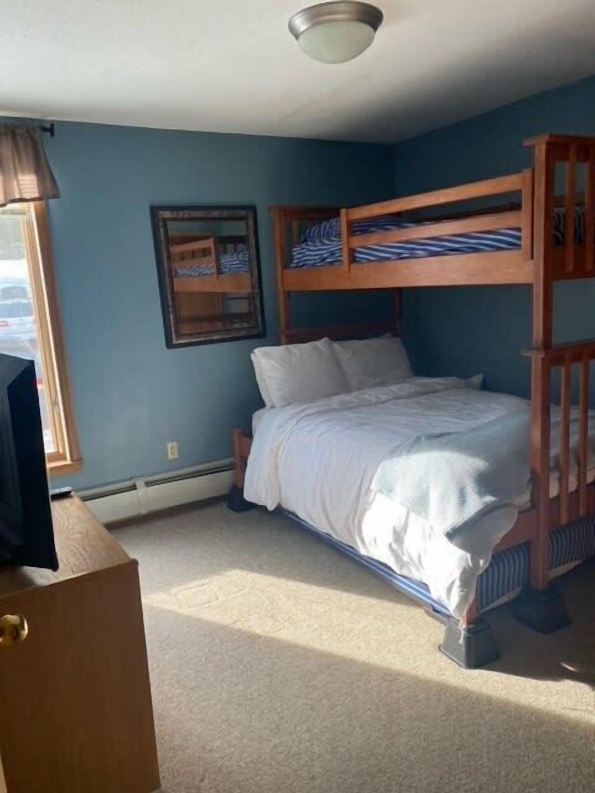 A bedroom with a bunk bed, a desk, and a window with curtains.