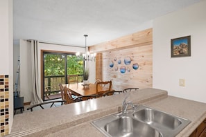 Una cocina con un lavamanos doble, paneles de madera en la pared y un comedor con mesa y sillas.