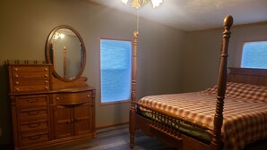 A bedroom with a wooden four-poster bed, a dresser with multiple drawers, a mirror, and a window with blinds. - Lodge at the Longbranch next to the Longbranch Saloon (AVA)