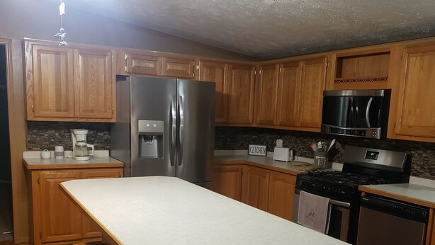 A kitchen with wooden cabinets, a stainless steel refrigerator, a microwave, a stove, and a dishwasher. There is a bar stool and a ceiling fan. - Lodge at the Longbranch next to the Longbranch Saloon (AVA)