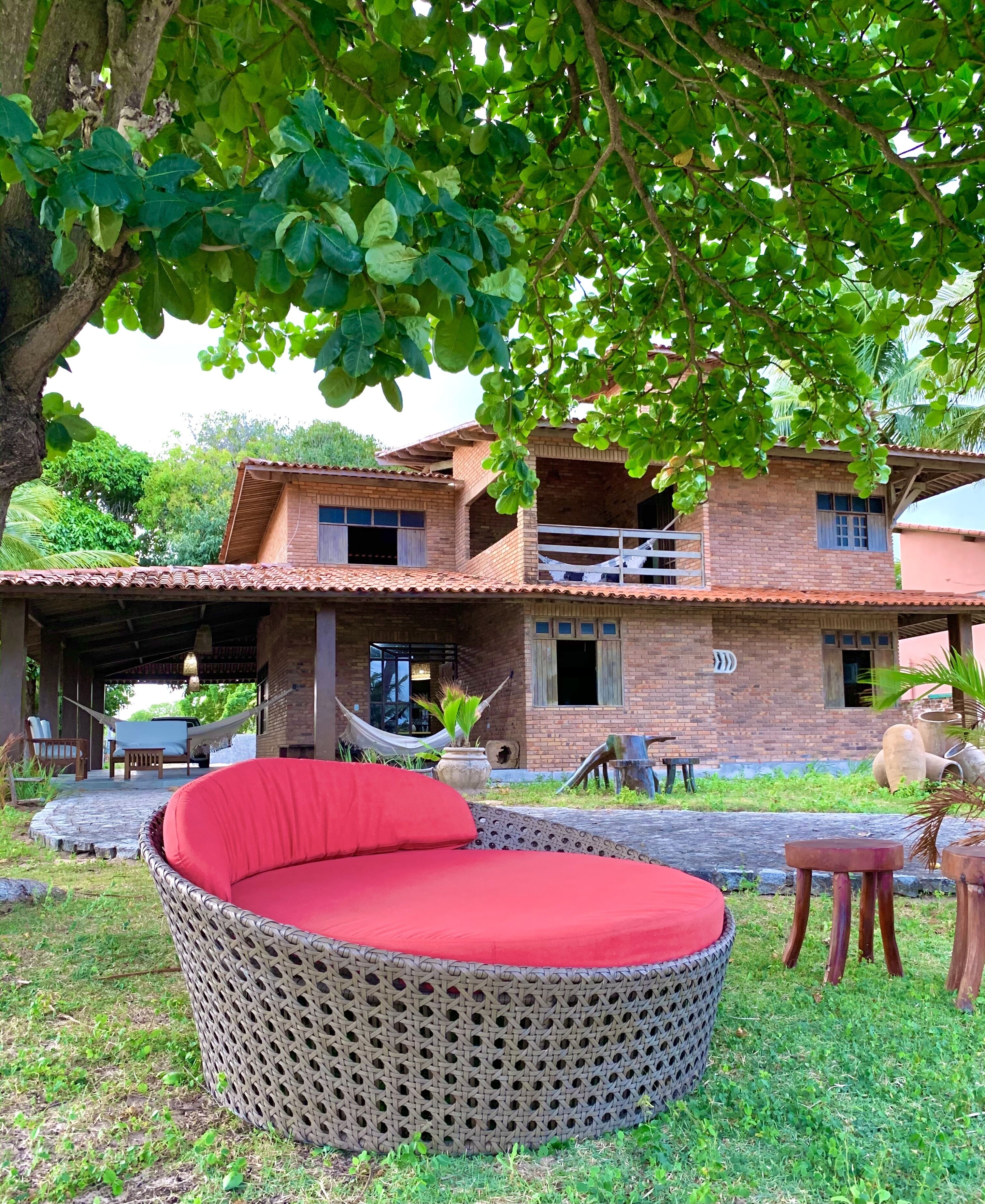 A two-story brick house with a covered patio, a red cushioned outdoor seating area, and a hammock.