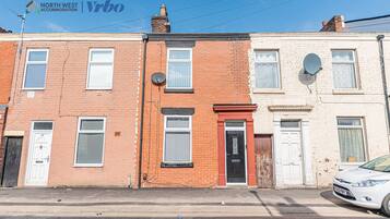 A row of terraced houses with a satellite dish, a car parked on the street, and a clear blue sky.