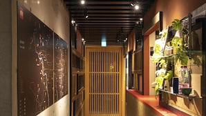 A narrow hallway with a wooden door, a map on the left wall, and a shelf with plants on the right. - HALE Kyoto Tambaguchi (Kyoto)