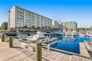 A marina with boats docked, a wooden pier, and a hotel with multiple balconies and a pool.