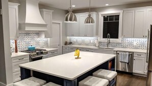 A modern kitchen with white cabinetry, a large island with bar stools, pendant lighting, and a patterned backsplash. - Luxury custom home long-stay family retreat in Shepherdstown (Shepherdstown)