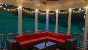 A covered outdoor seating area with a red sofa and a coffee table, string lights, and a view of a green landscape. - Luxury custom home long-stay family retreat in Shepherdstown (Shepherdstown)