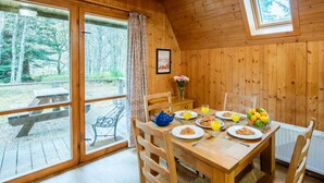 A wooden cabin with a dining table set for breakfast, a bench outside, and a view of the forest. - Rowan Cottage by Interhome (Drumnadrochit)