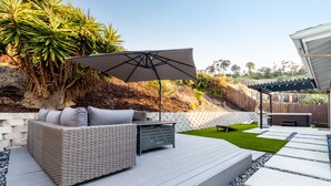 Eine Terrasse mit Rattan-Sofa, Sonnenschirm und einer Steinmauer.