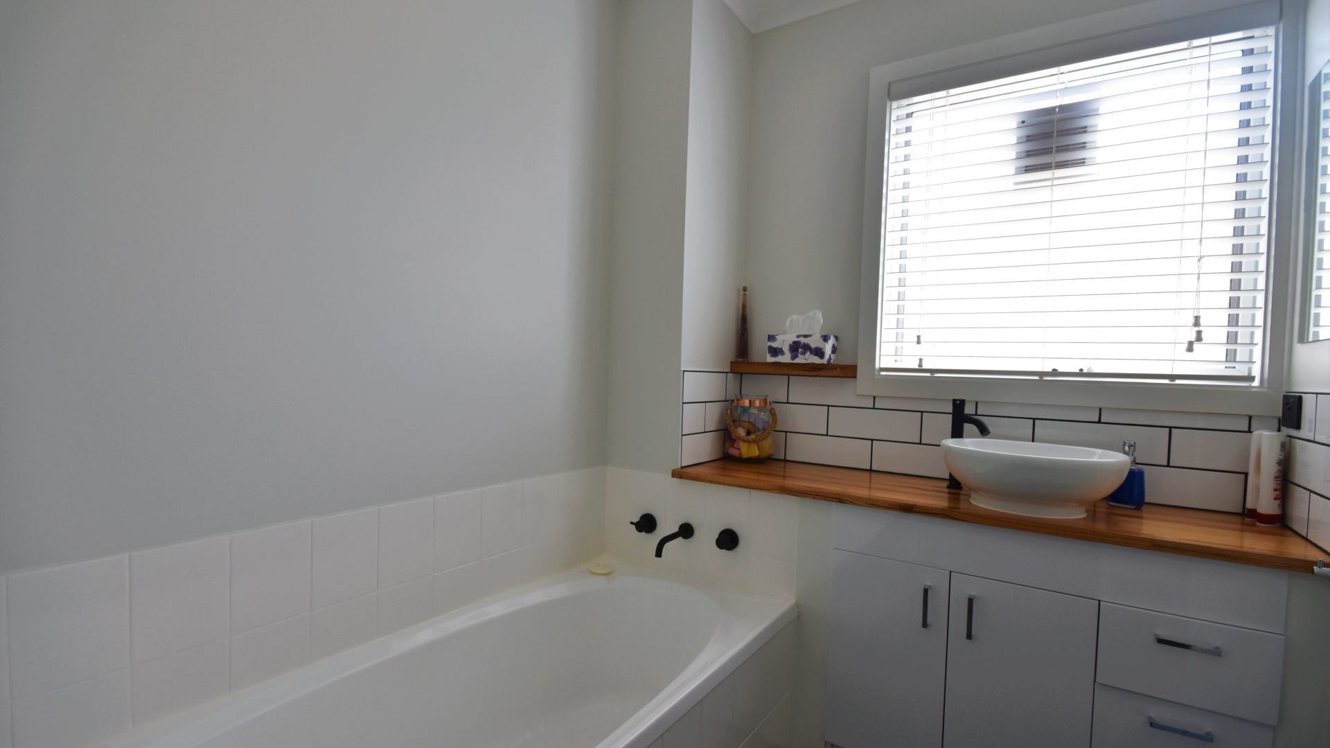 A modern bathroom with a freestanding bathtub, a white sink, and a window with blinds.
