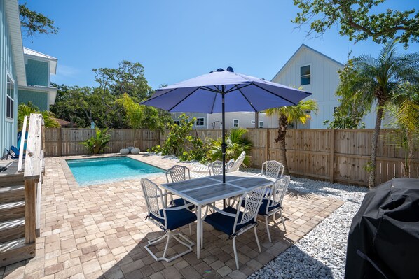 Un patio trasero con piscina, muebles de jardín y valla de madera.