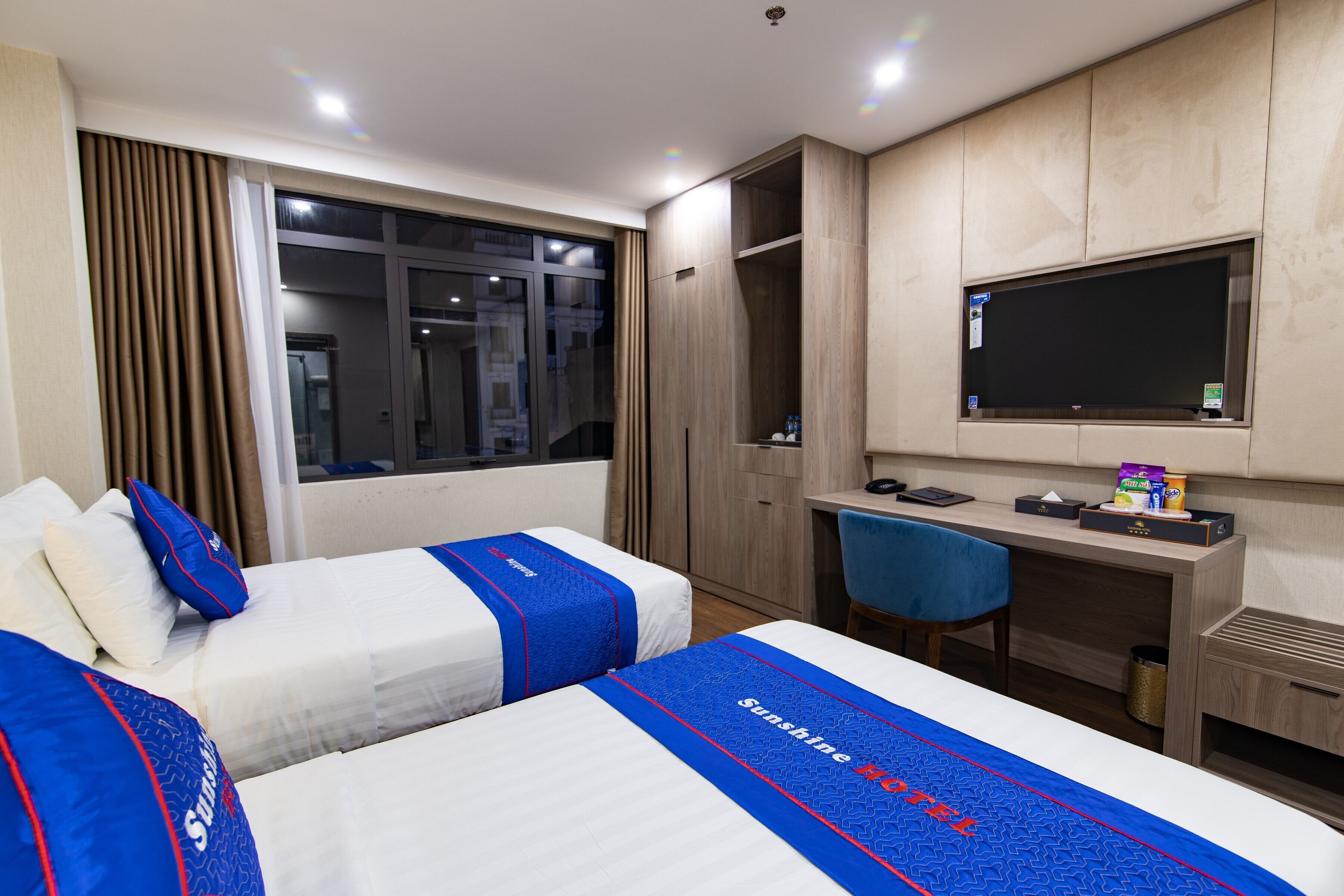 A hotel room with two beds, a desk, a chair, a TV, and a wardrobe.