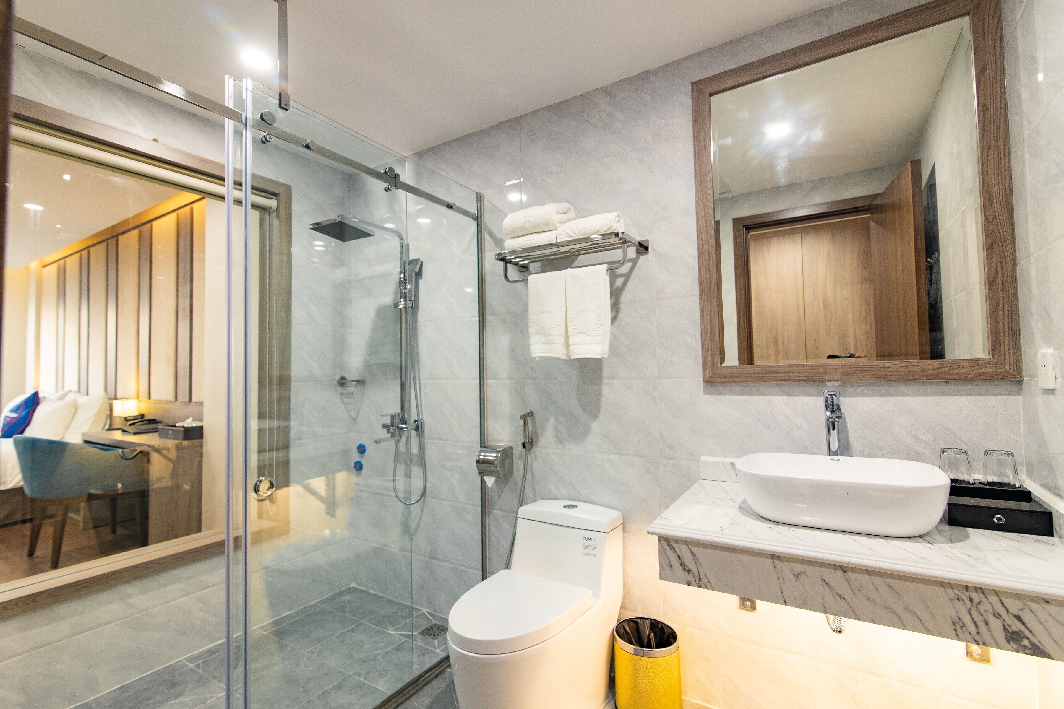 A modern bathroom with a glass-enclosed shower, a toilet, a sink with a marble countertop, and a large mirror above the sink.