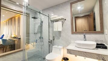A modern bathroom with a glass-enclosed shower, a toilet, a sink with a marble countertop, and a large mirror above the sink.
