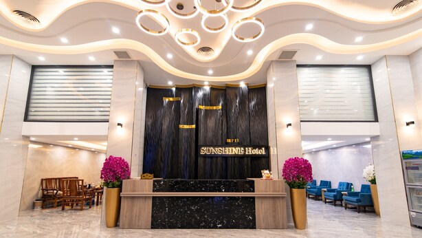 En receptionsdisk i sort marmor, to store store krukker med planter, og et skilt med teksten "Sunshine Hotel".