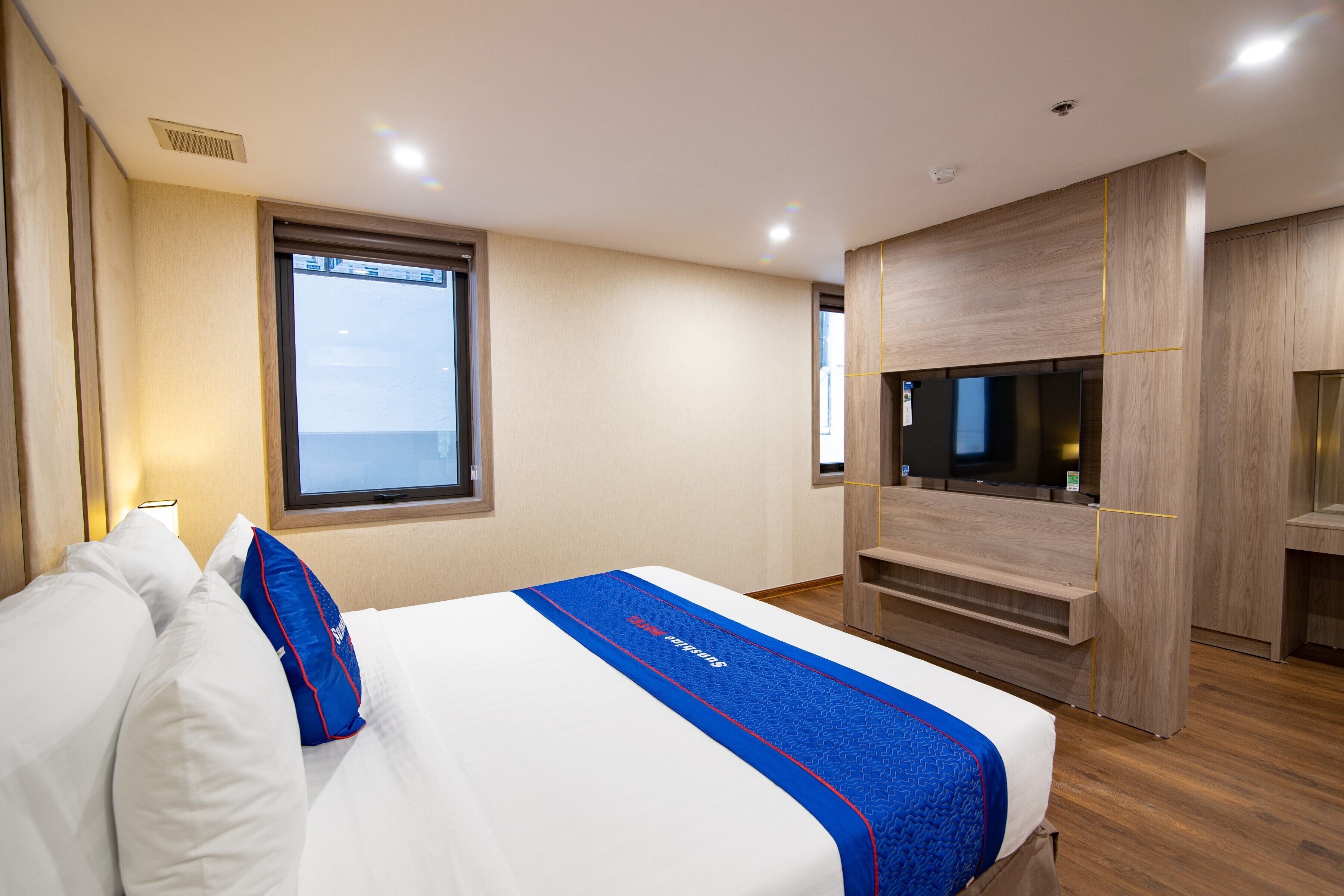A modern hotel room with a large bed, a TV, and a window providing a view of the sky.
