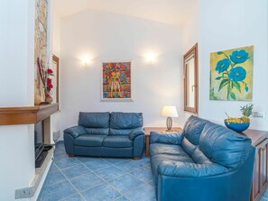 A living room with two blue leather sofas, a small table with a lamp, and artwork on the walls.