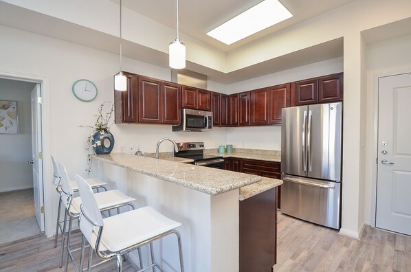 A modern kitchen with dark wooden cabinets, stainless steel appliances, and a central island with bar stools.