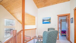 A spacious living area with a high ceiling and wooden beams, a comfortable armchair, a small table, and a view of a bedroom with a bed and a window. - On the river close to all adventure and short drive to Durango (D&S Train/Mesa Verde/Million Dollar HWY) (Bayfield)