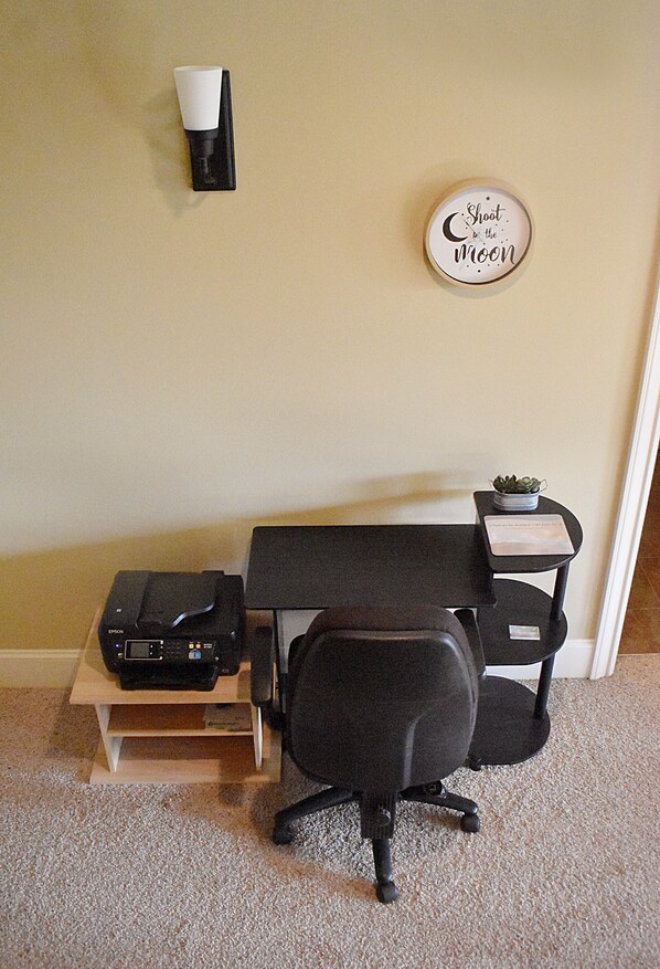 A small office space with a desk, chair, printer, and a wall-mounted sign.