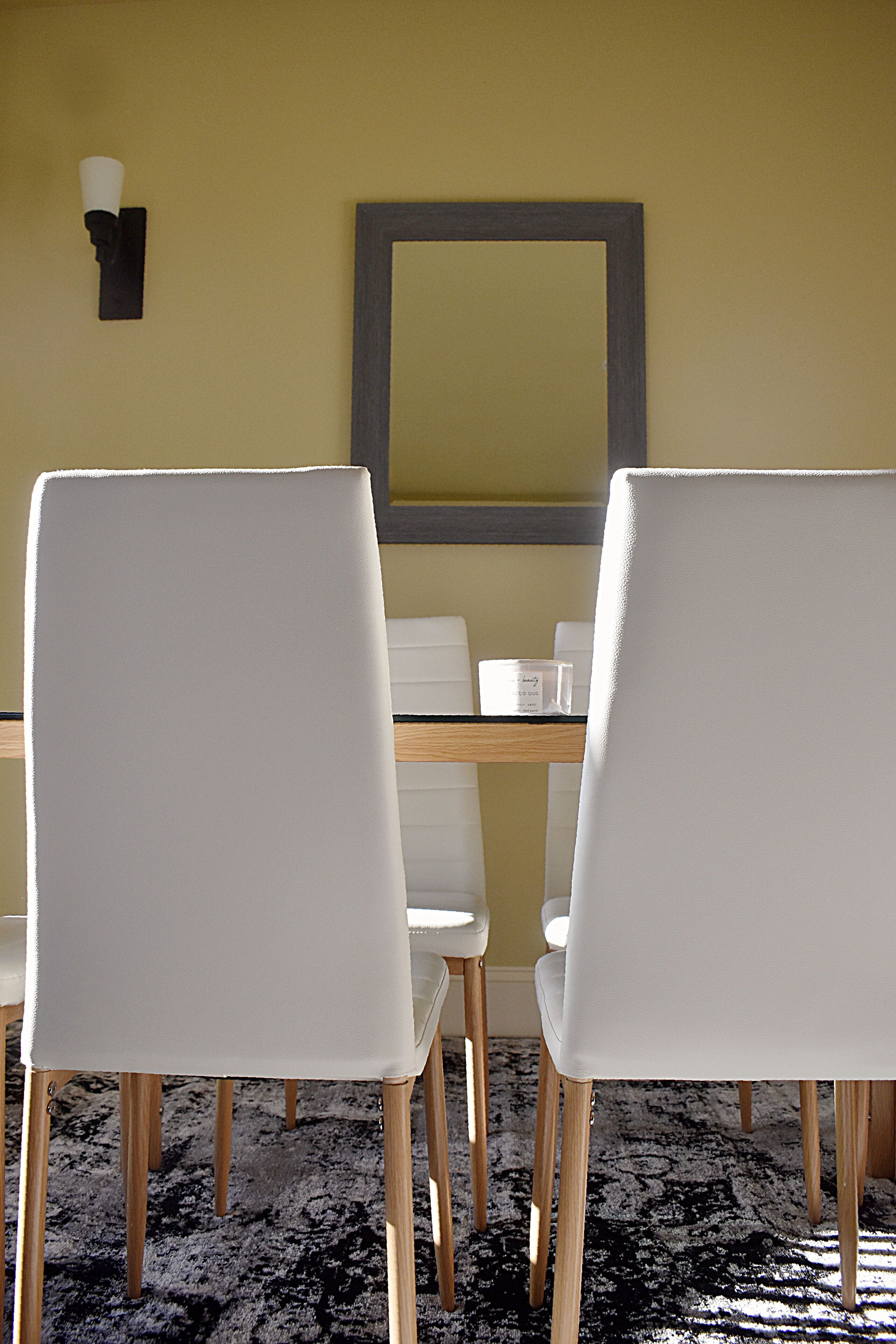 Un comedor con dos sillas blancas, una mesa de madera y una lámpara fijada a la pared.