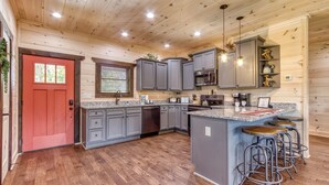 A modern kitchen with grey cabinets, a red door, and a bar area with stools. - Modern Smoky Mtn Cabin, Hot Tub, Game Room, Pool Table, Near Dollywood (Sevierville)
