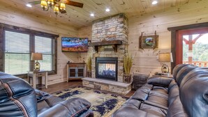 A cozy living room with a stone fireplace, leather sofas, and a television mounted on the wall. - Modern Smoky Mtn Cabin, Hot Tub, Game Room, Pool Table, Near Dollywood (Sevierville)