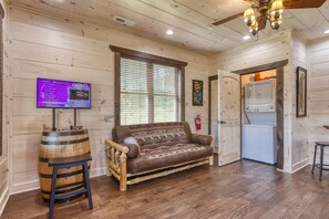 Ein gemütliches Blockhaushaus-Interieur mit Holzboden, einer rustikalen Couch, einem Fernseher und einer Küchenzeile.