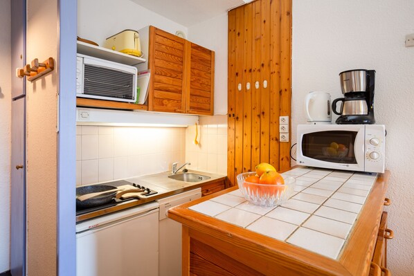 Een kleine keuken met een magnetron, koffiezetapparaat en een fruitschaal op het aanrecht.