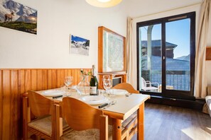 Un coin repas avec une table en bois dressée pour quatre personnes, une grande fenêtre donnant sur une montagne et une carte encadrée accrochée au mur.
