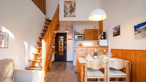 A cozy interior with a wooden staircase, a dining area with a table set for two, and a kitchen with wooden cabinets and appliances. - Cham Sud Balme401 Family 2BR Walk to Lifts & Centre, Chamonix, France (Chamonix)