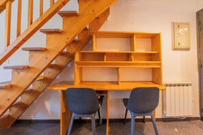 Een houten bureau met twee stoelen, een houten trap en een radiator aan de muur.