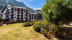 A multi-story building with balconies, a grassy courtyard, and a mountain backdrop. - Cham Sud Balme401 Family 2BR Walk to Lifts & Centre, Chamonix, France (Chamonix)