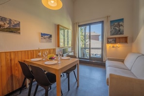 A dining area with a wooden table set for four, a white sofa, and a view through a glass door to the outside.