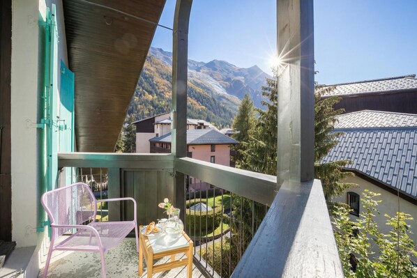 Un balcon avec vue sur les montagnes, une chaise, une table avec un vase et des fleurs, et une balustrade.