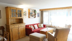 Een gezellige woonkamer met een rode bank, een houten kast en een beige fauteuil.