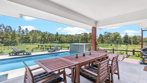 Ein Poolbereich mit Holztisch und Stühlen, einem Grill und Blick auf eine natürliche Landschaft.