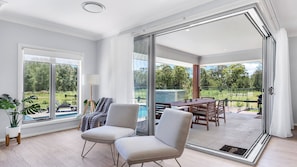 Ein geräumiges Zimmer mit einem großen Schiebeglasfenster, das zu einem Außenbereich mit Pool und Esstisch führt.