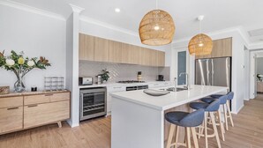Eine moderne Küche mit weißen Schränken, einer zentralen Kochinsel, Barhocker, einem eingebauten Backofen und einem Edelstahl-Kühlschrank.