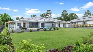 A modern two-story house with a well-maintained lawn, a patio with outdoor furniture, and a large garage. - KOKOON - THE VINTAGE HOLIDAY HOUSES (POKOLBIN)
