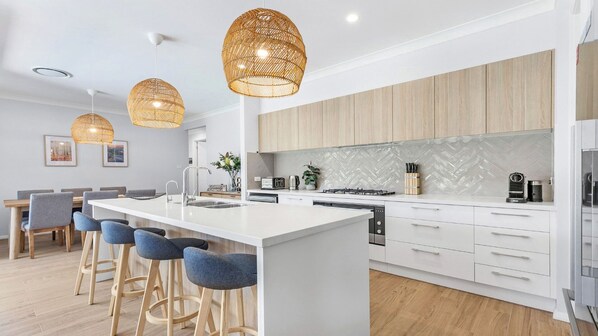 A modern kitchen with a central island, bar stools, and pendant lighting. - KOKOON - THE VINTAGE HOLIDAY HOUSES (POKOLBIN)
