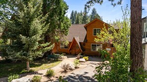A wooden cabin with a sloped roof, surrounded by dense trees and a gravel driveway. - Mallard Landing Lakefront - Log Cabin, Lakeside, Foosball, Lake Views (Big Bear Lake)
