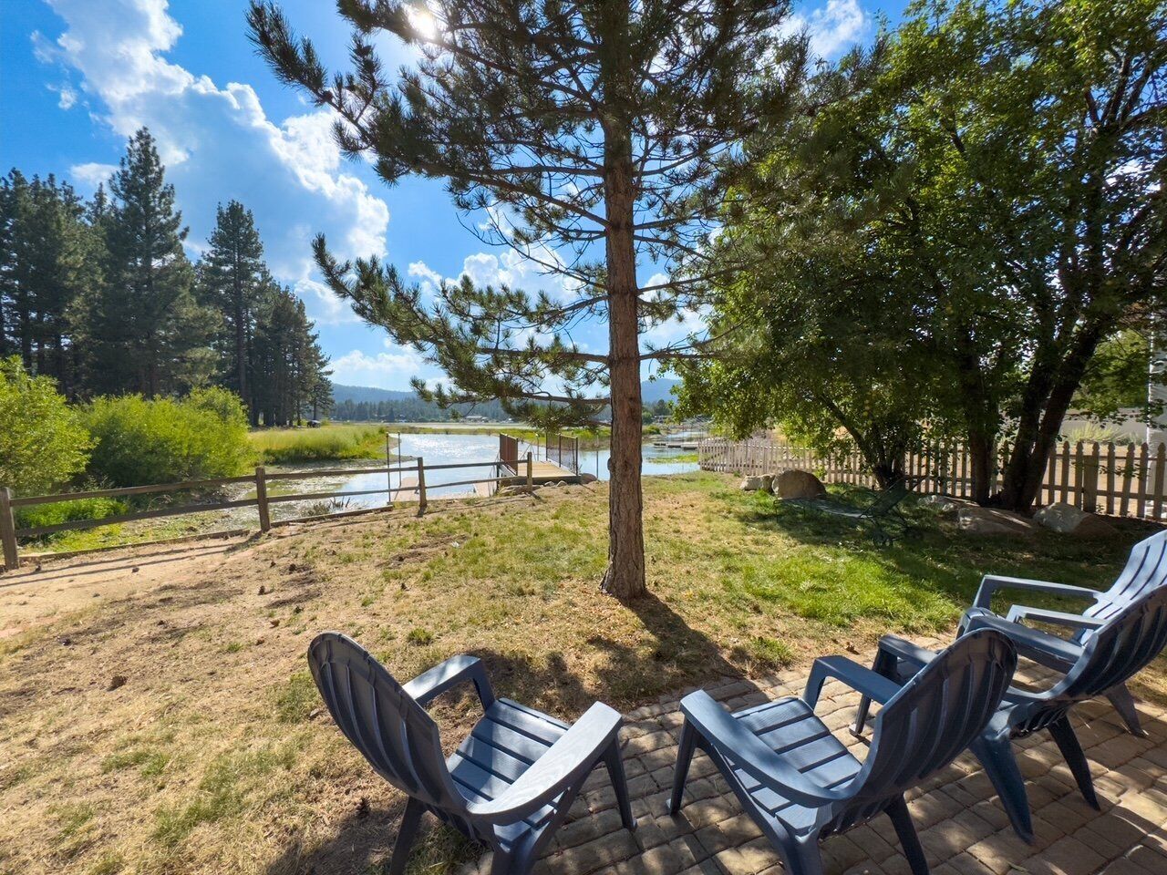 Eine Terrassenfläche mit zwei Liegestühlen, die auf einen Fluss ausgerichtet ist, umgeben von Bäumen und einem Holzzaun.